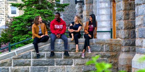 A group of four young people sitting on a stone wall.
